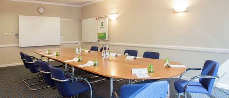 A conference room with a long table, blue chairs, a whiteboard, and a clock on the wall.