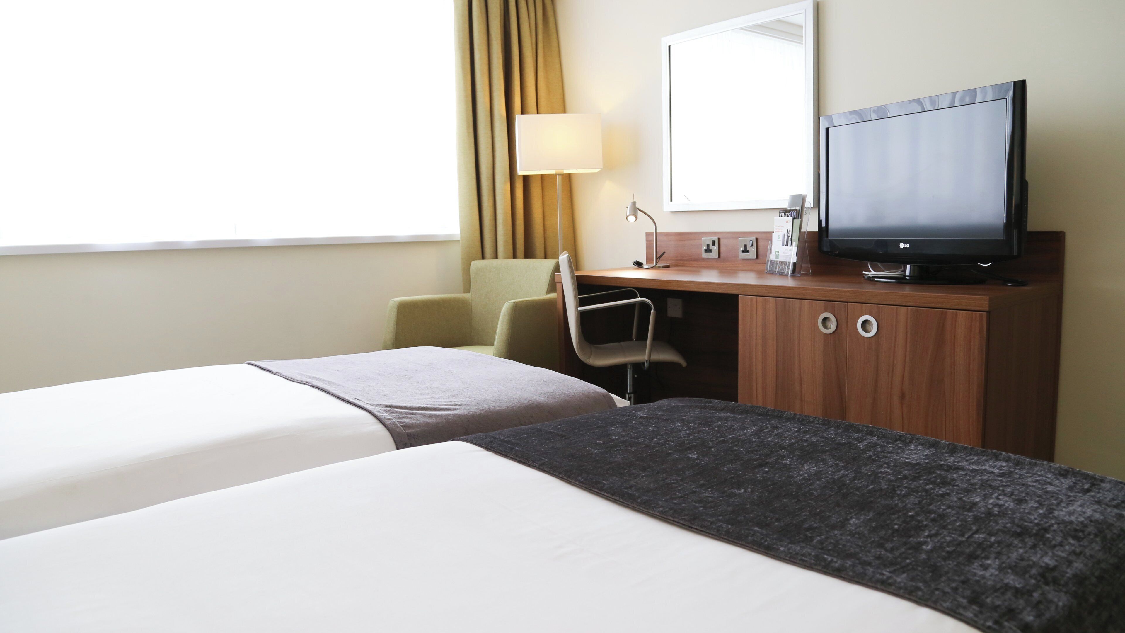 A hotel room with two beds, a desk with a television, and a chair.