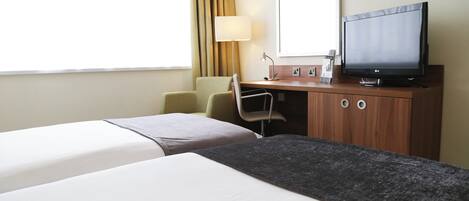 A hotel room with two beds, a desk with a television, and a chair.