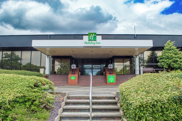 A Holiday Inn hotel entrance with a covered walkway, accessible entrance sign, and a staircase leading up to the entrance.
