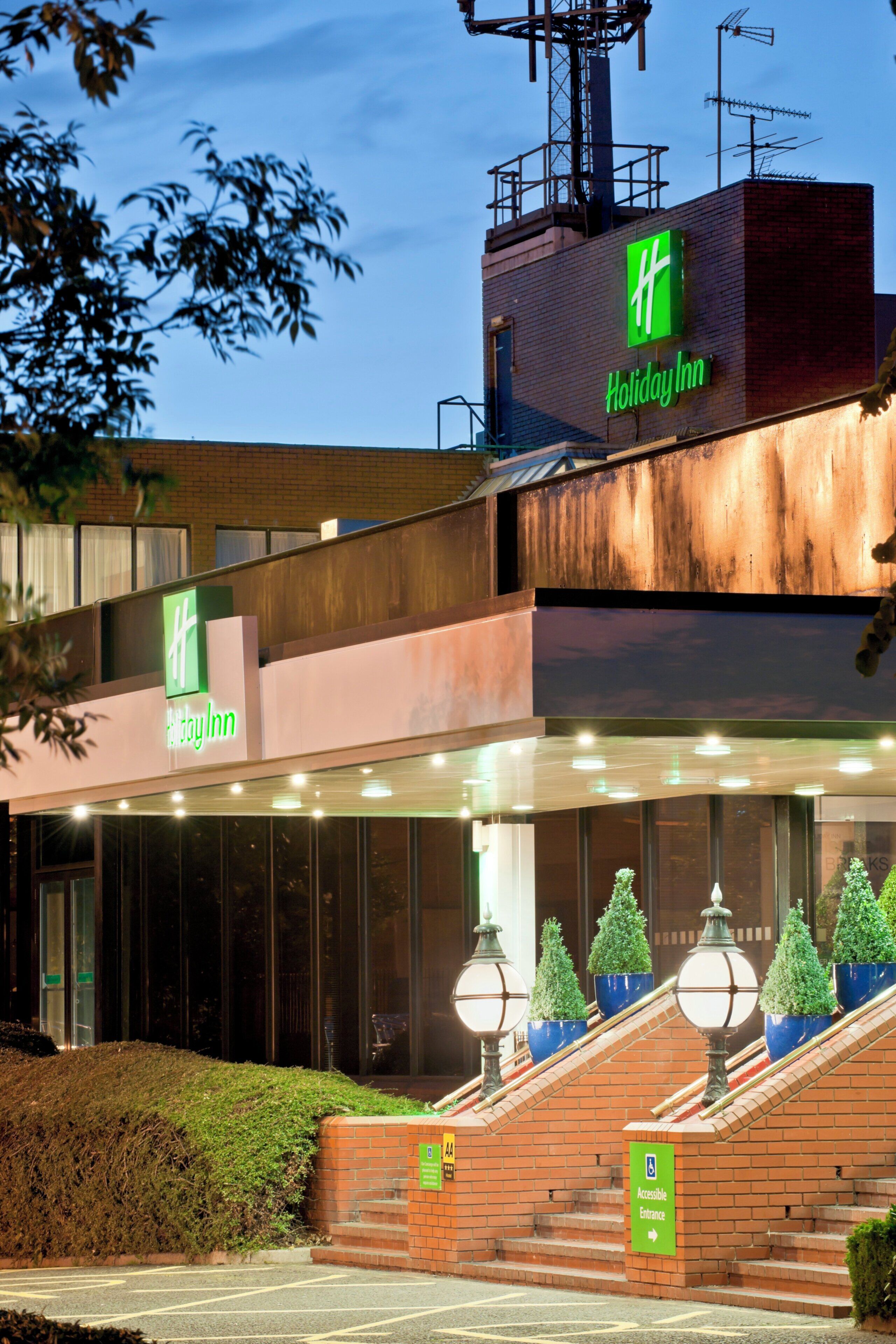 Un hotel Holiday Inn con fachada de ladrillo, un acceso cubierto y una escalera que lleva al edificio principal.