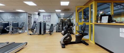 A gym with various exercise equipment, a reception desk, and a sign indicating a members area.