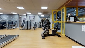 Une salle de sport équipée de divers appareils d’exercice, un comptoir d’accueil et un panneau indiquant l’accès réservé aux membres.