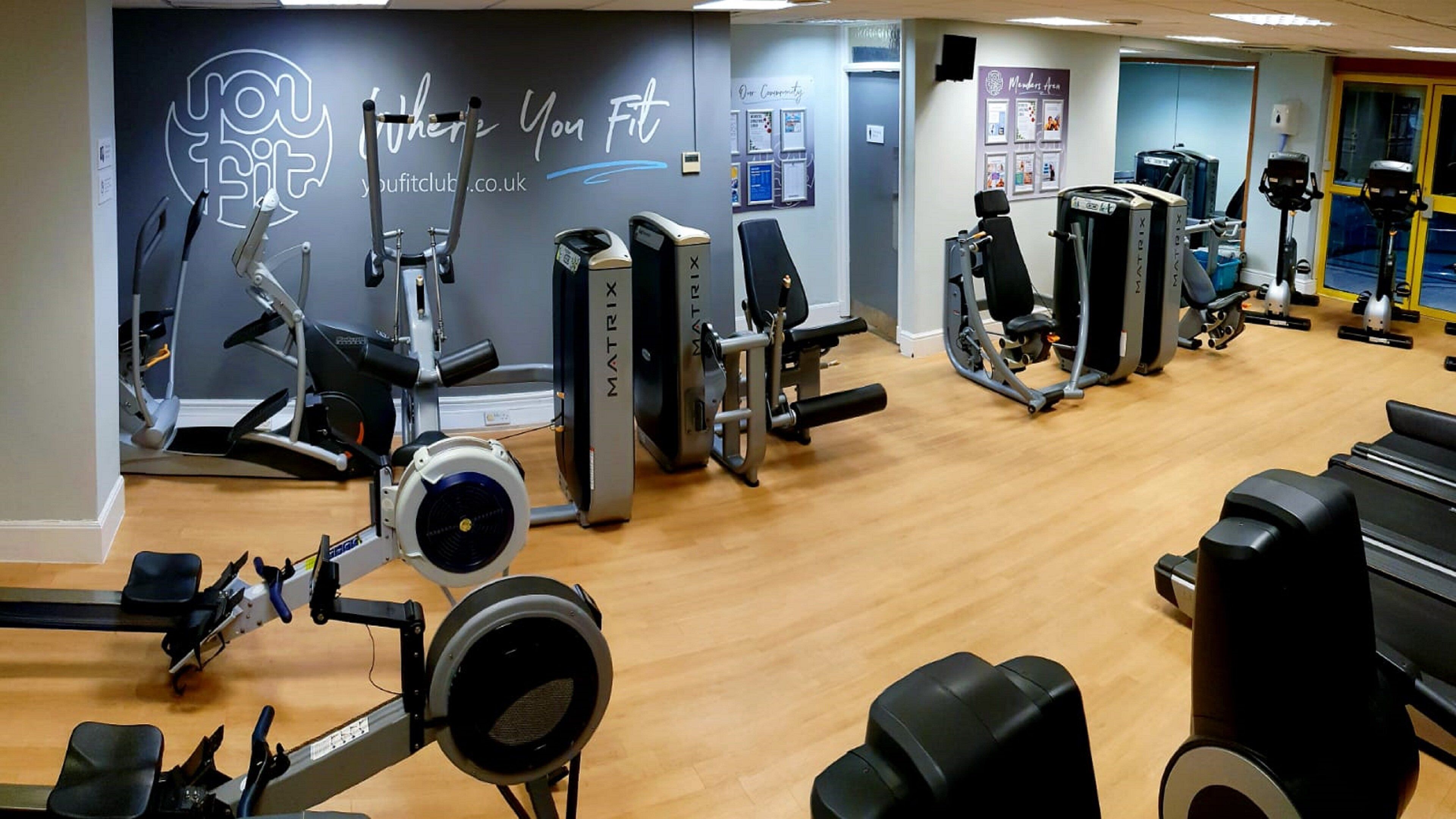 A gym with various exercise machines, a wooden floor, and a wall with motivational text.