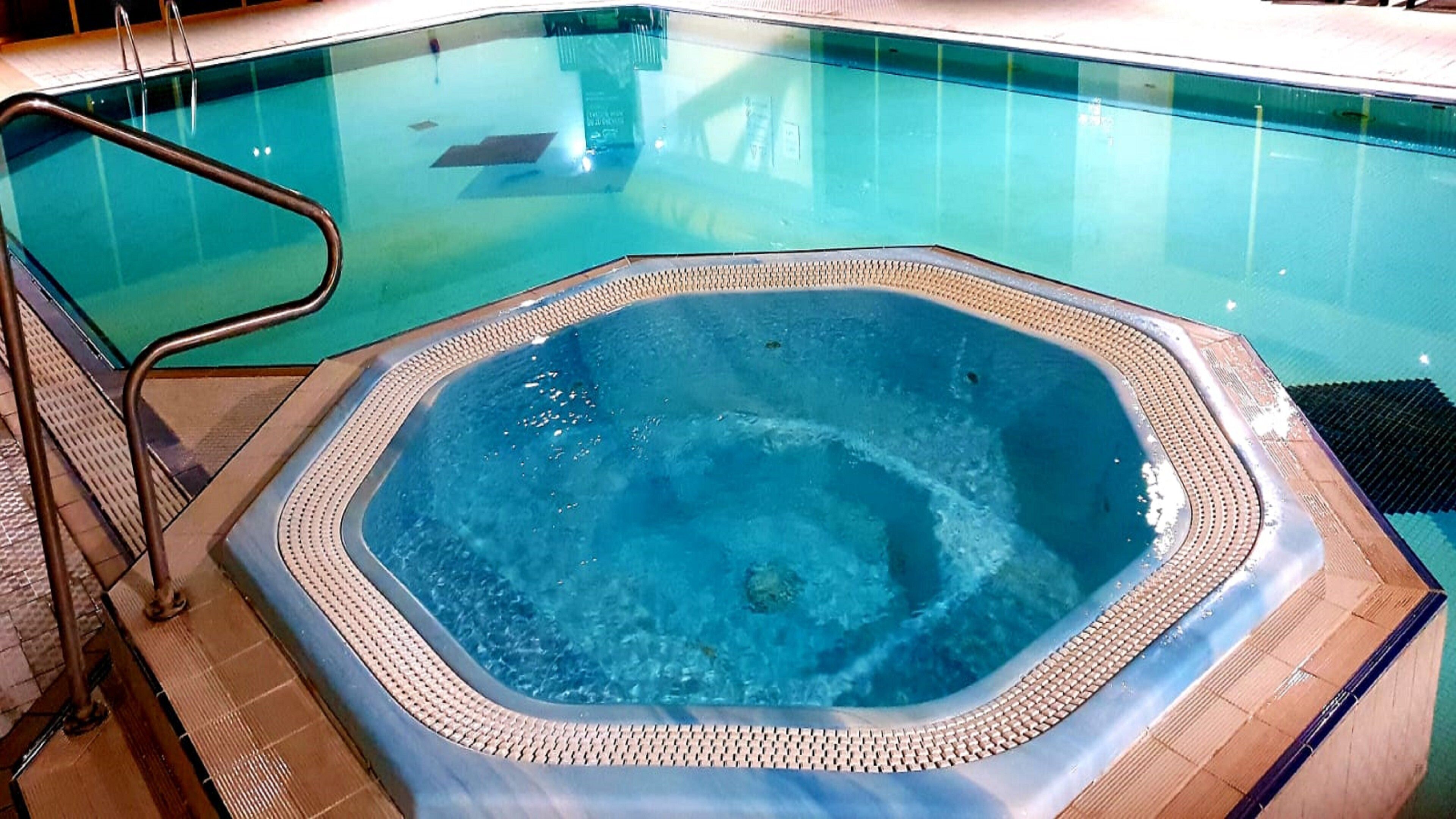 Un bain à remous doté d’une terrasse carrelée et de rampes en métal.