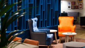 A modern interior with a blue partition, a blue armchair, an orange armchair, and a small round table. - Holiday Inn Runcorn by IHG (Runcorn)
