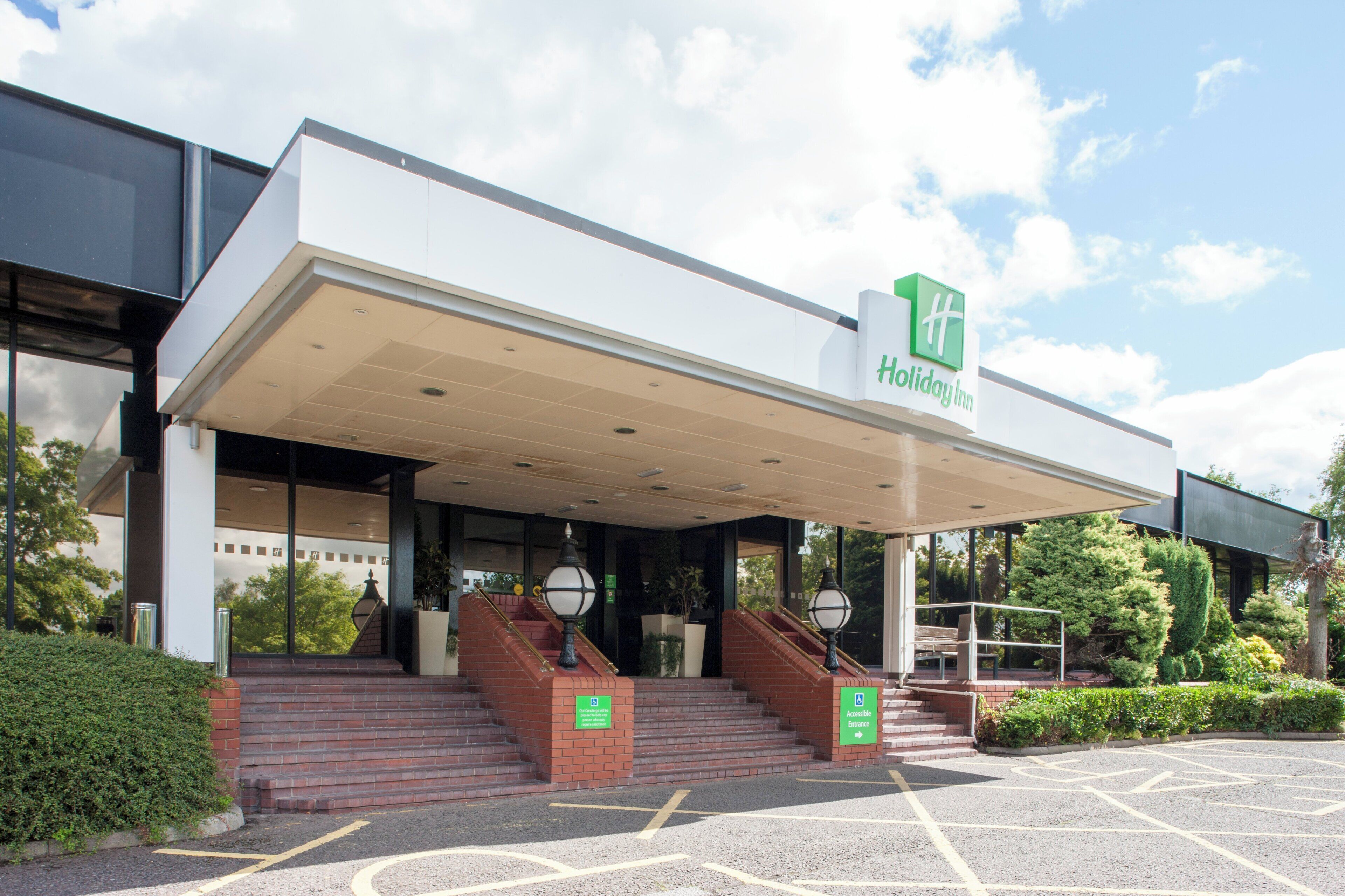 Entrada de un hotel Holiday Inn con un vestíbulo techado, acceso para personas con movilidad reducida y un área de estacionamiento.