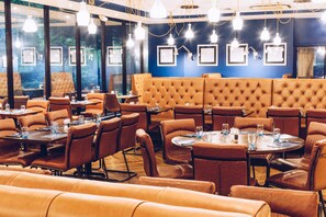 A restaurant with leather booths and tables, framed pictures on the walls, and hanging pendant lights.