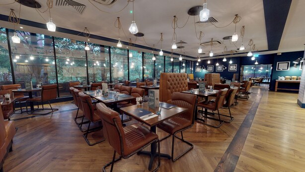 A restaurant with wooden tables and chairs, large windows, and hanging pendant lights. - Holiday Inn Runcorn by IHG (Runcorn)