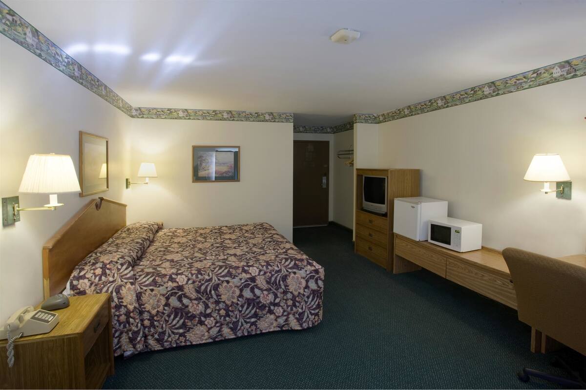 A hotel room with a bed, bedside lamps, a desk with a microwave, a chair, and a telephone.