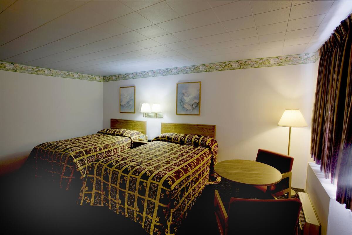 A hotel room with a double bed, two bedside lamps, a round wooden table, and a chair.
