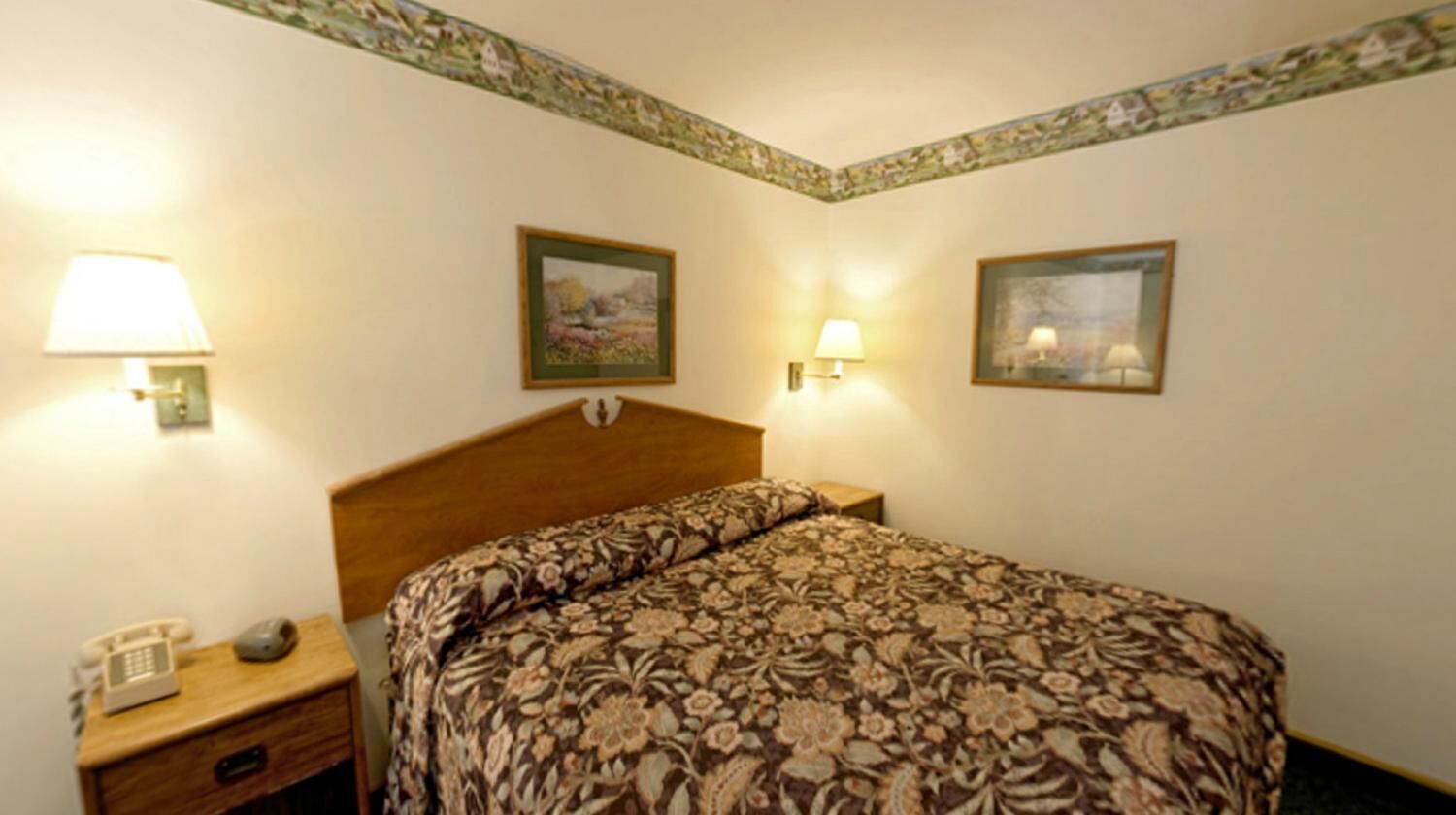 A hotel room with a bed, two bedside lamps, a nightstand with a telephone, and two framed pictures on the wall.