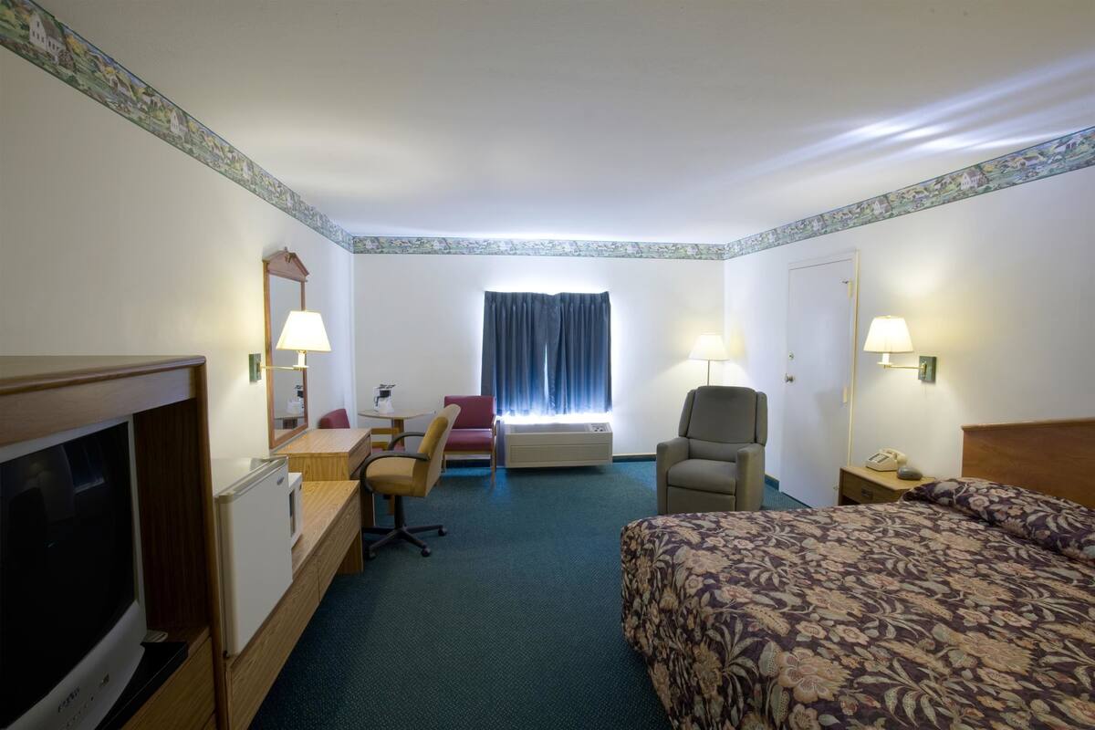 A hotel room with a bed, desk, chair, TV, and a window with curtains.