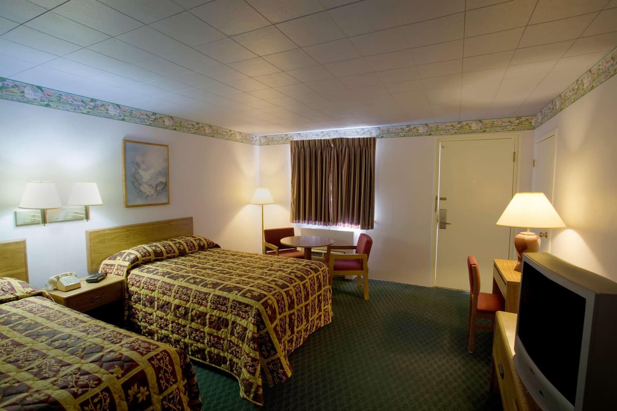 A hotel room with a bed, two bedside tables with lamps, a desk with a chair, a television, and a door.