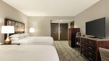 A hotel room with two beds, a TV, a desk with a coffee maker, and a painting on the wall.