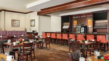 A hotel lobby with a bar area, seating arrangements, and a coffee station.