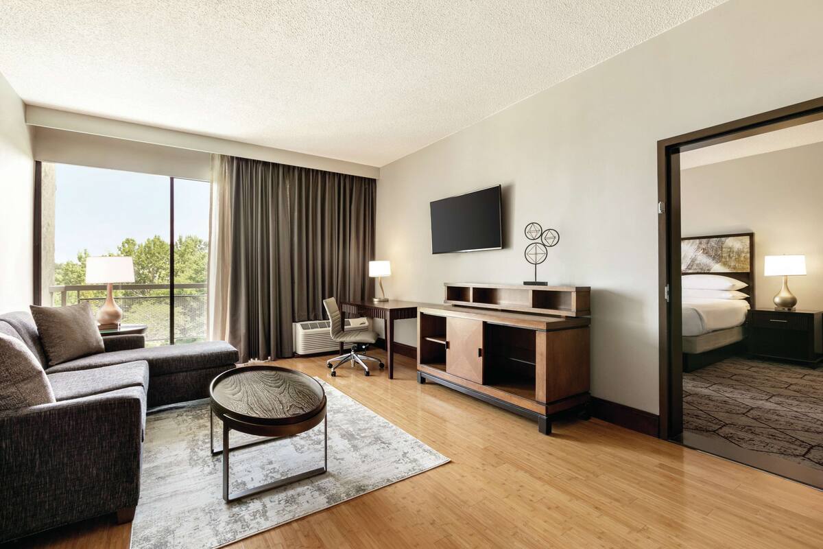 A hotel room with a sofa, desk, TV, and a bed.