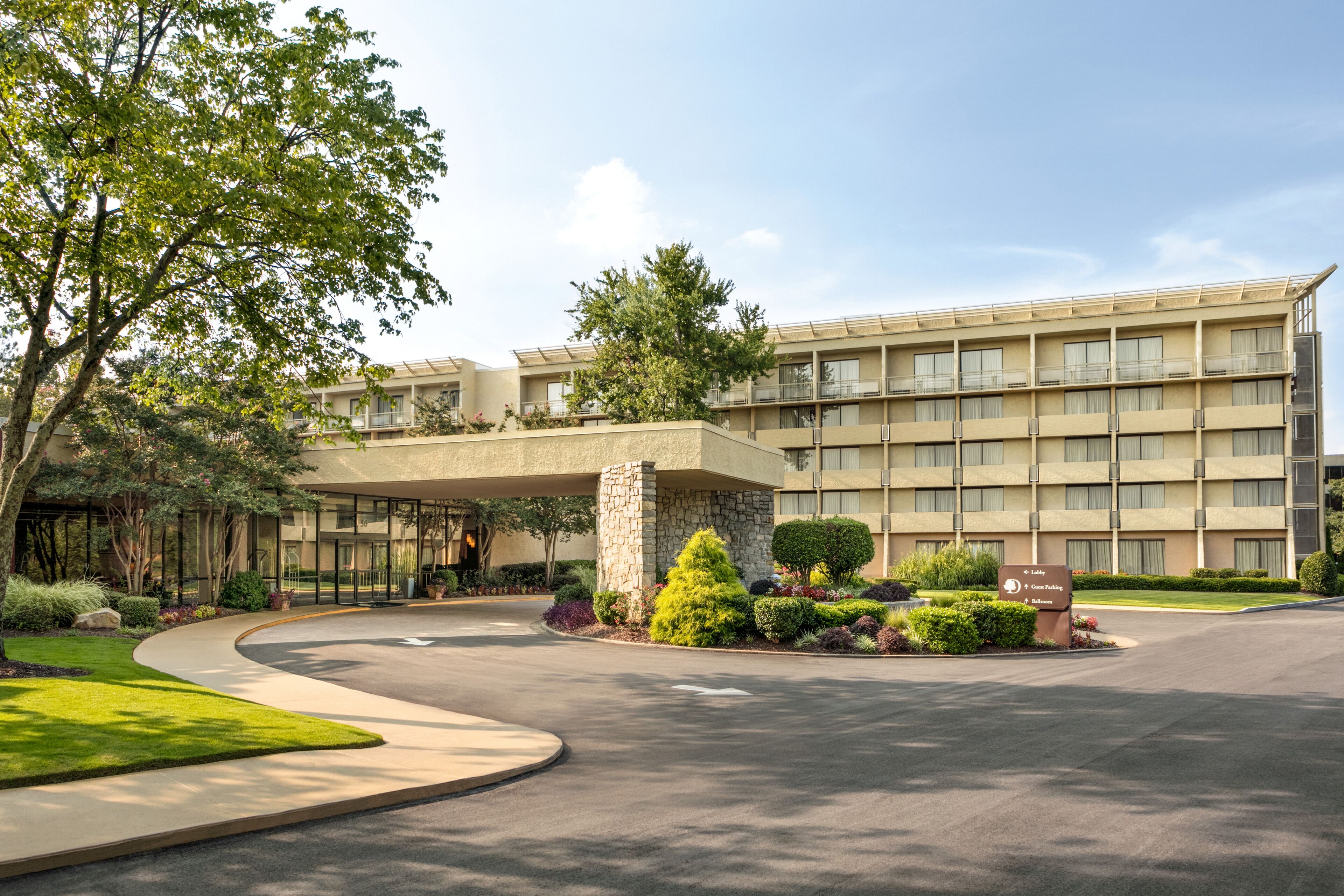 A hotel with a modern design, featuring a curved driveway, landscaped gardens, and a multi-story building with balconies.