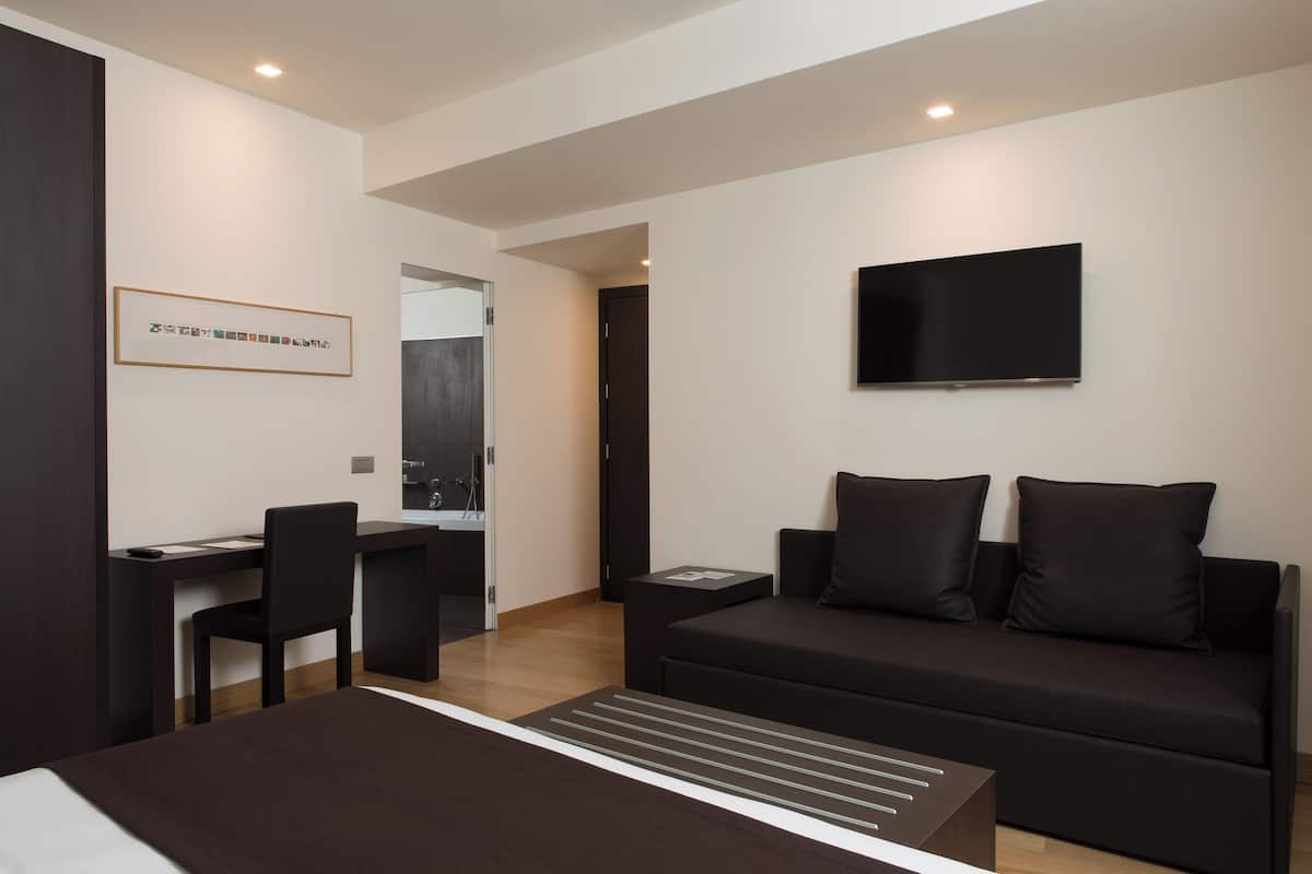 Une chambre d’hôtel moderne équipée d’un lit, d’un bureau, d’une chaise, d’un canapé et d’une télévision.