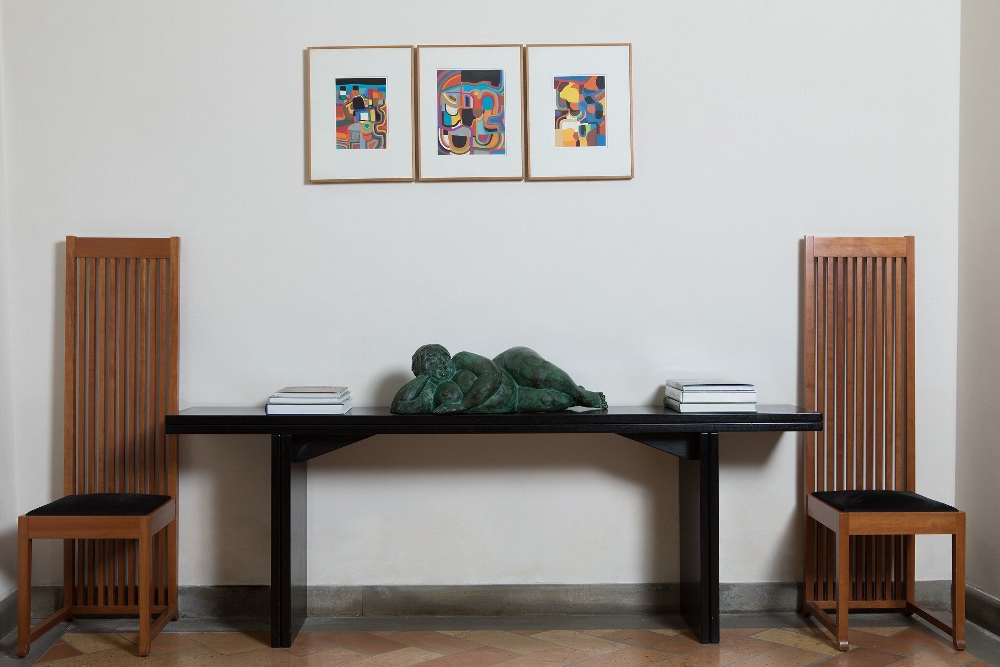 Ein Zimmer mit einem schwarzen Tisch, zwei Holzstühlen und drei gerahmten abstrakten Bildern an der Wand.