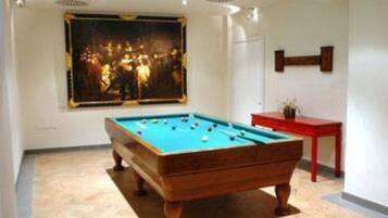 Una mesa de billar en una habitación con un cuadro grande en la pared y una mesita lateral roja.