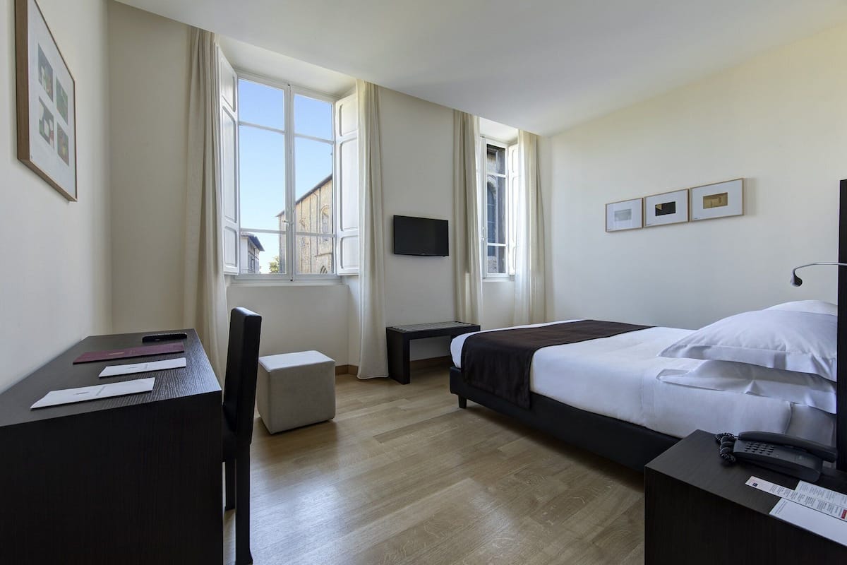 Une chambre d’hôtel équipée d’un lit, d’un bureau, d’une chaise, d’une télévision et d’une fenêtre avec des rideaux.