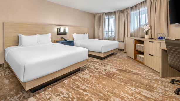 A hotel room with two beds, a desk, a TV, and a window with curtains.