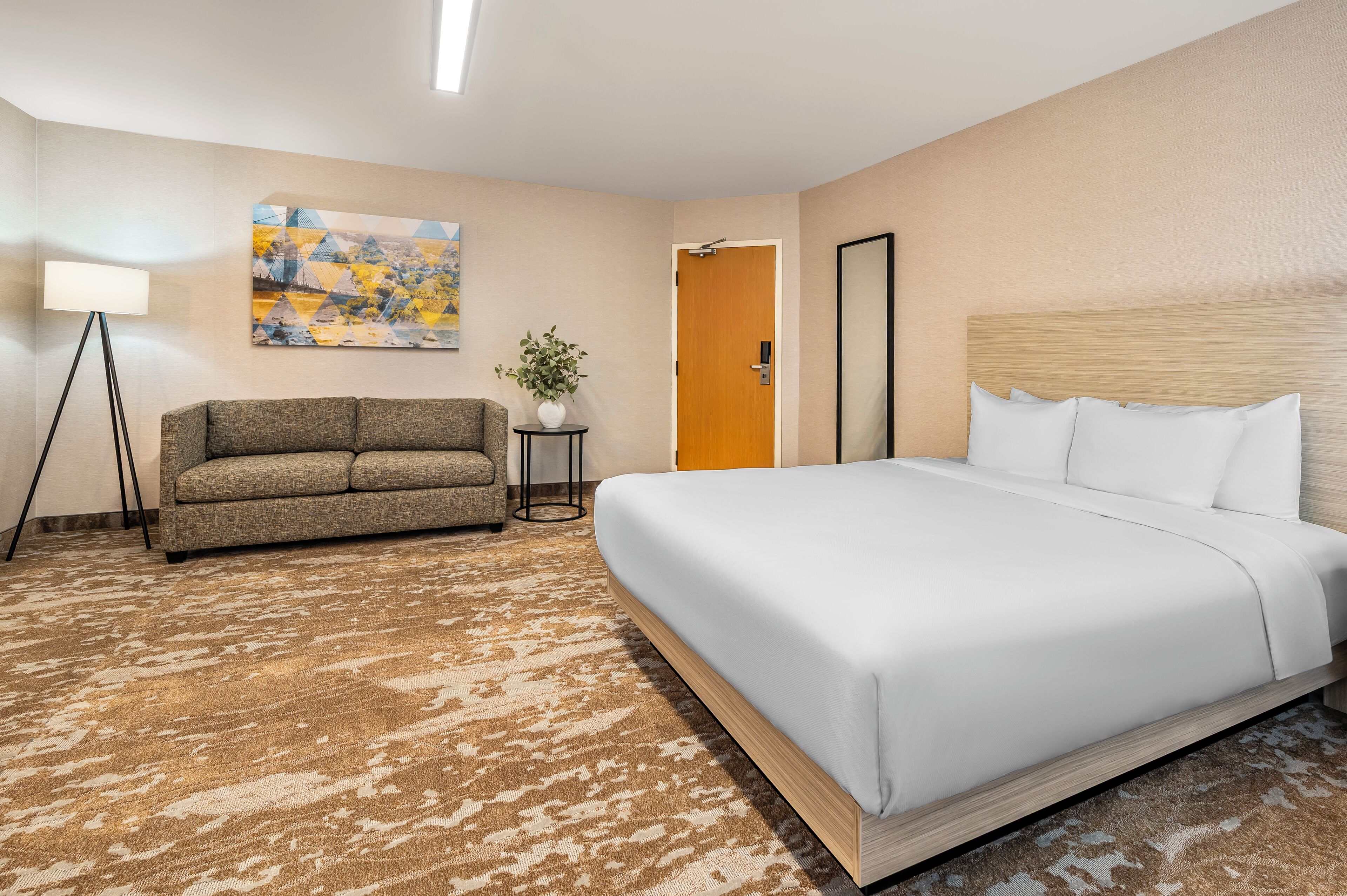 Une chambre d’hôtel avec un grand lit, un canapé, une petite table avec une plante et un tableau au mur.