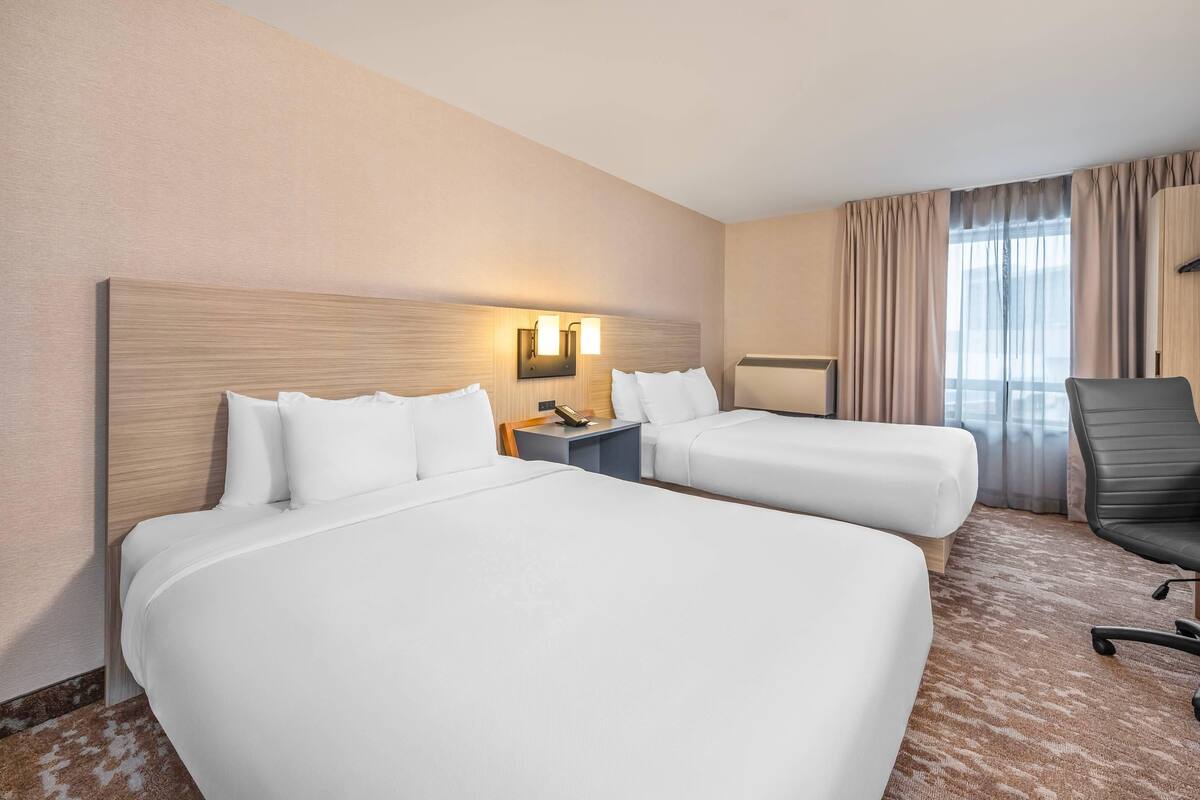 A hotel room with two beds, a nightstand, a desk, a chair, and a window with curtains.