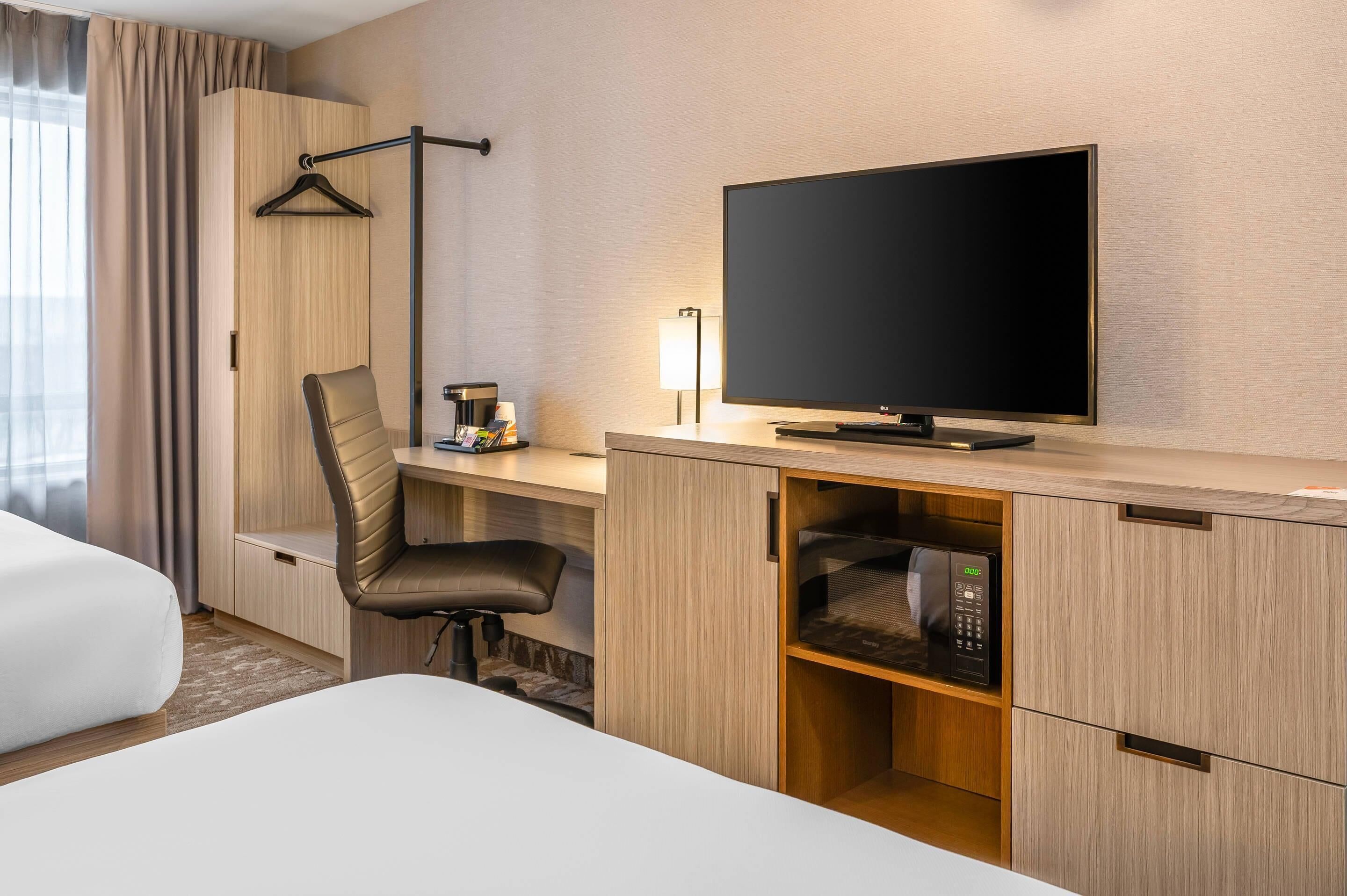 Habitación de hotel con cama, escritorio con televisor, silla, lámpara y microondas.