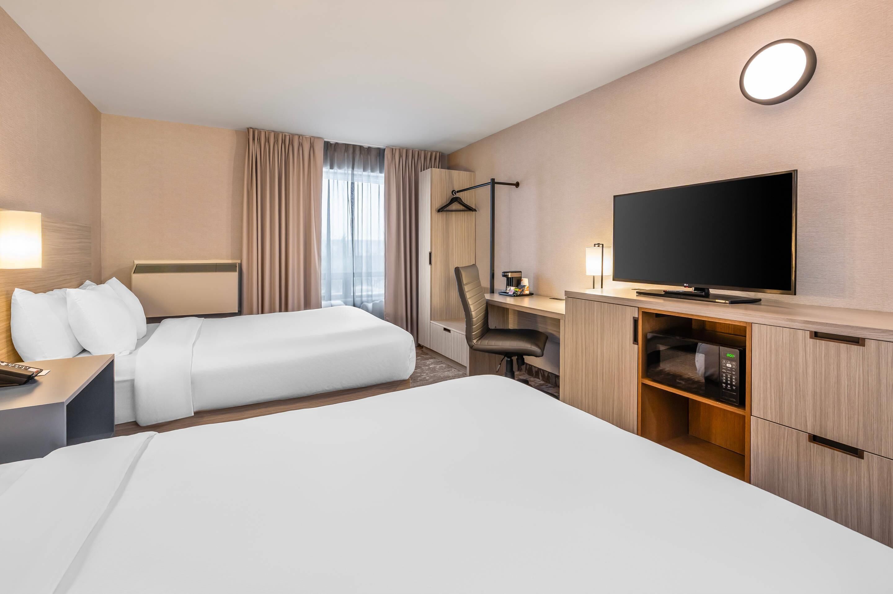 A hotel room with two beds, a desk with a flat-screen TV, a chair, and a wardrobe.