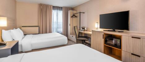 A hotel room with two beds, a desk with a flat-screen TV, a chair, and a wardrobe.