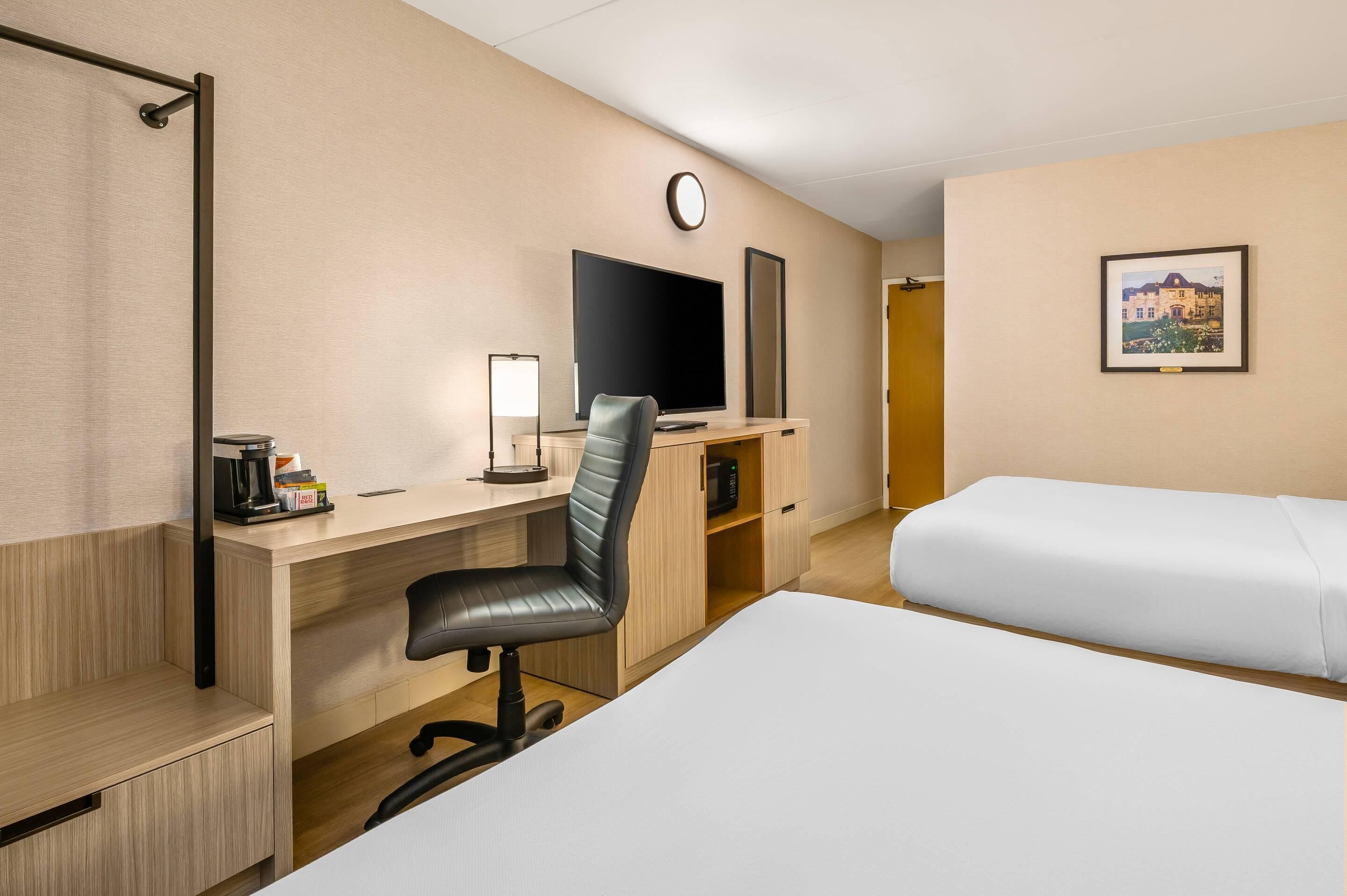 A hotel room with a desk, chair, TV, bedside tables, and two beds.
