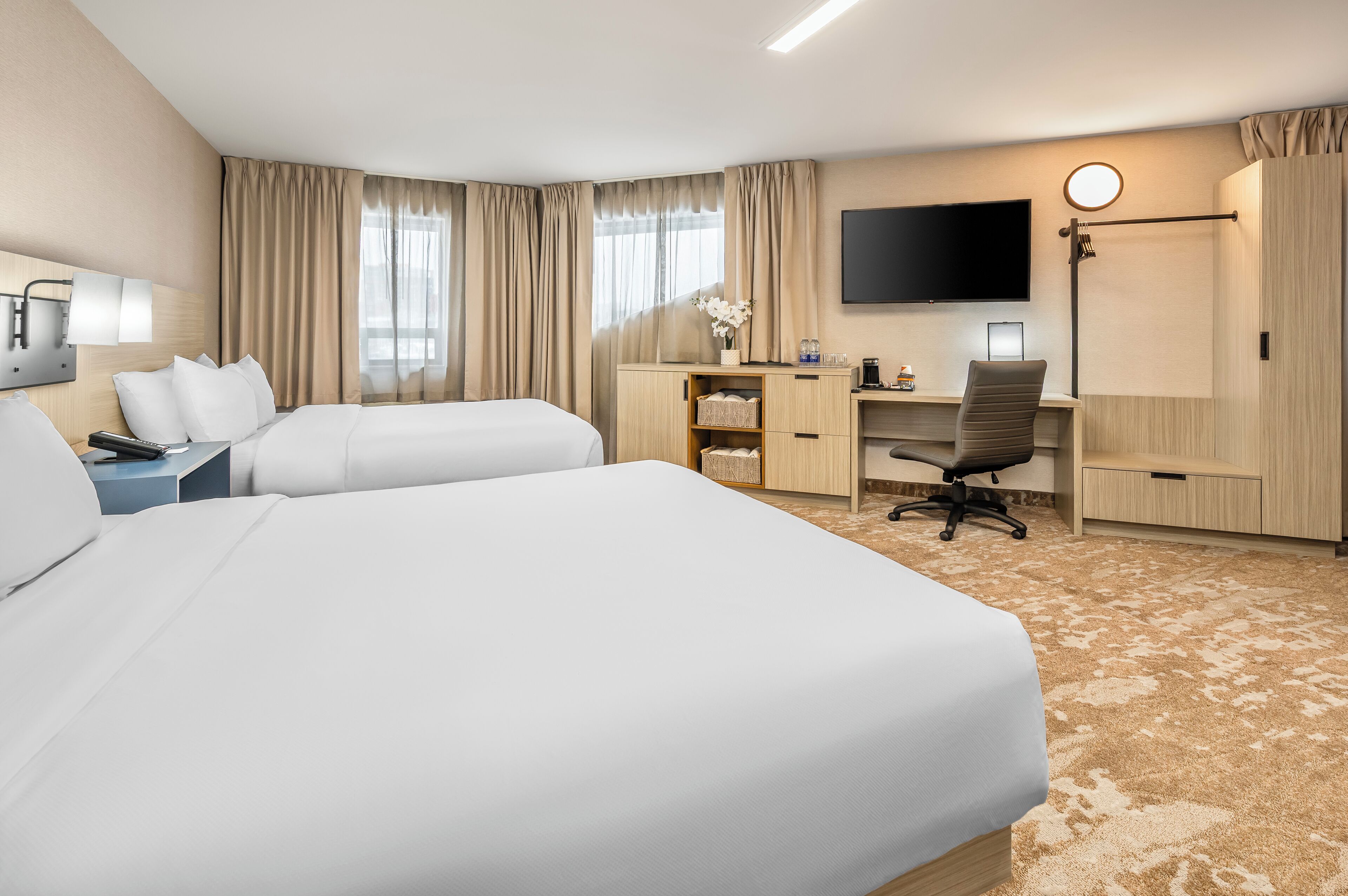 Une chambre d’hôtel avec deux lits, un bureau, une chaise, une télévision et une armoire.