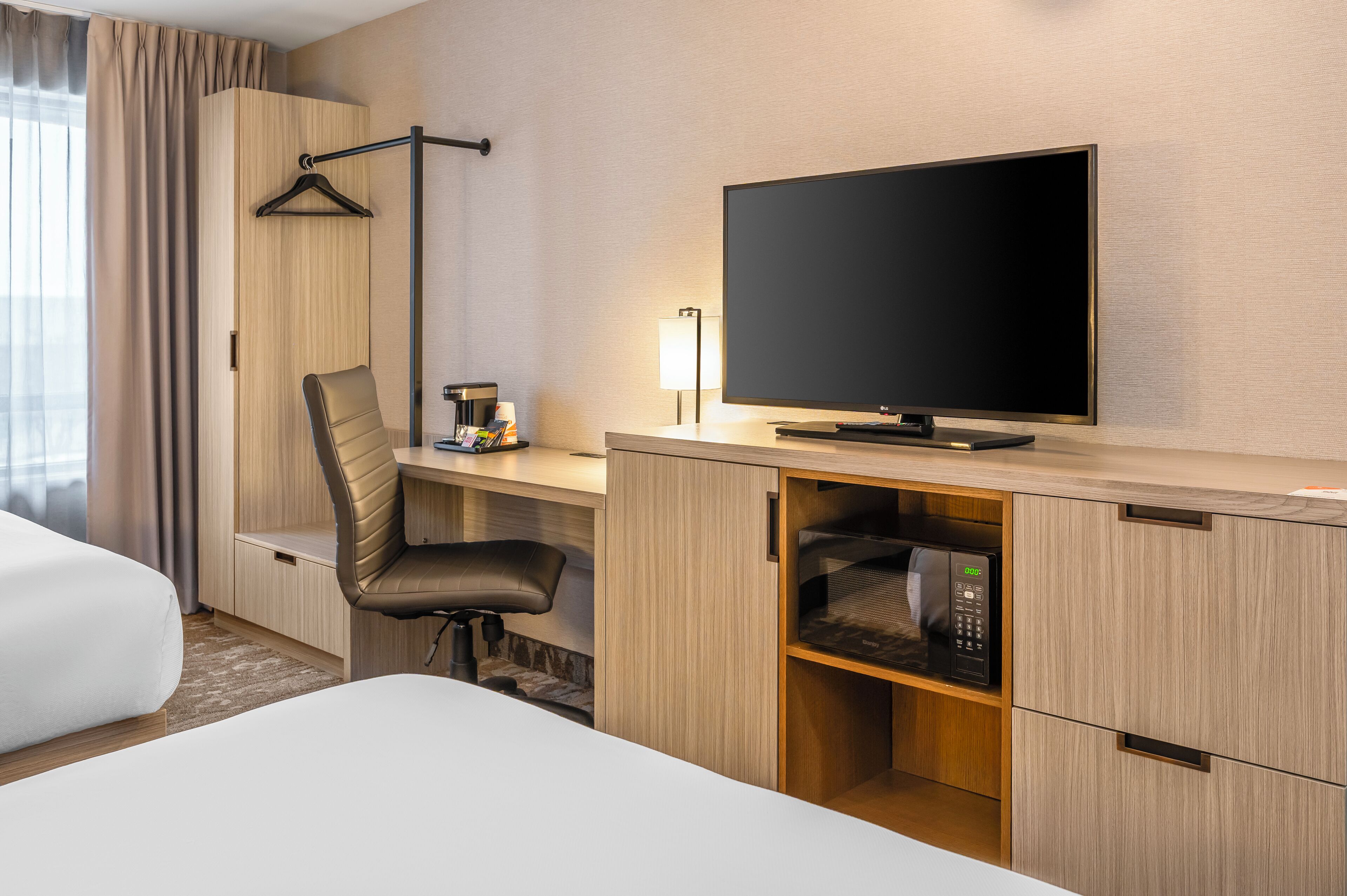 A hotel room with a bed, a desk with a chair, a television, a lamp, and a microwave.