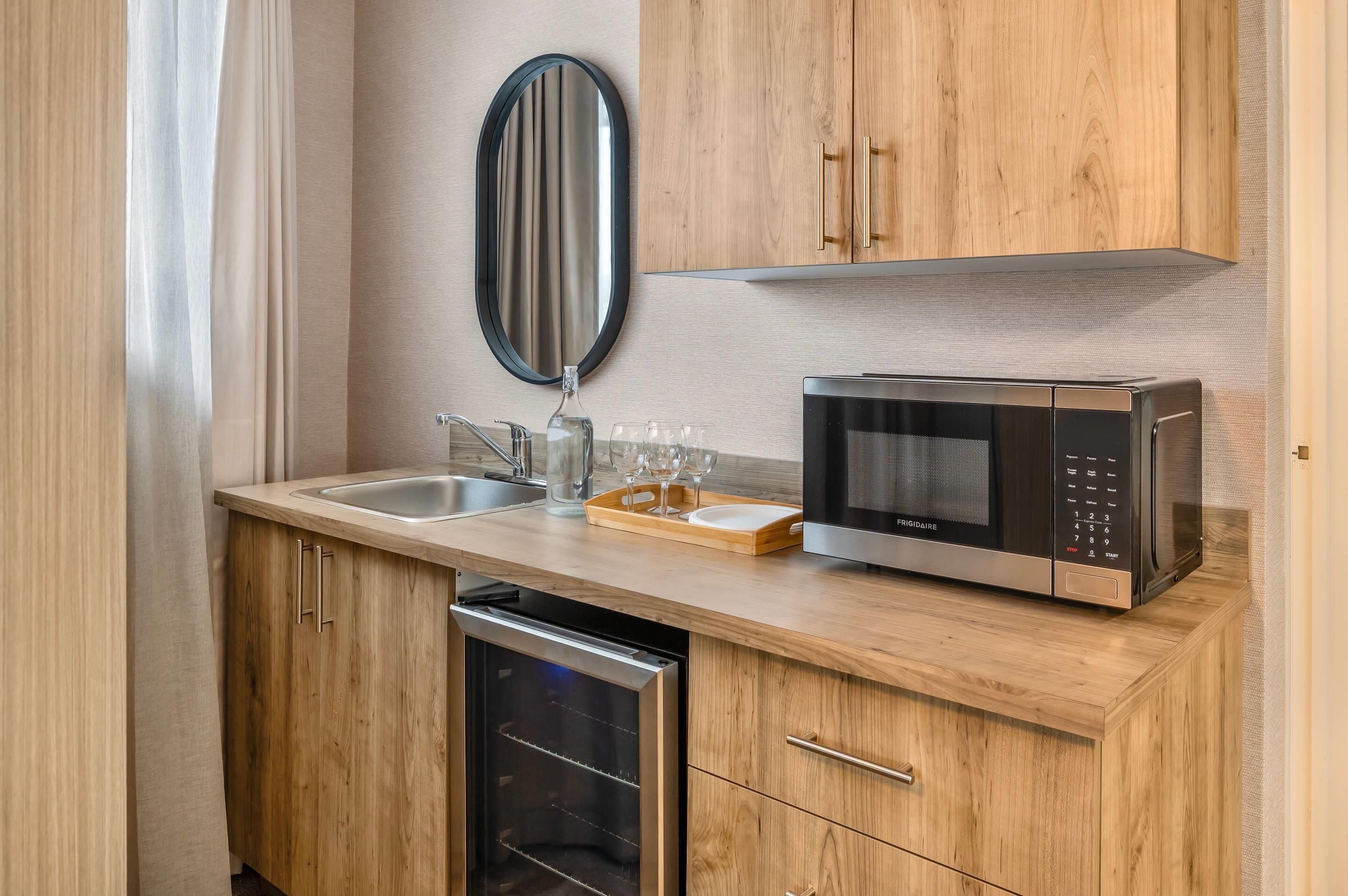 A compact kitchen with wooden cabinets, a stainless steel sink, a microwave, and a dish drying rack.