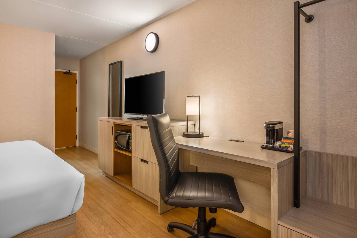 A hotel room with a bed, a desk with a chair, a television, a lamp, and a coffee maker.