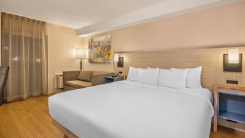 Habitación de hotel con una cama grande, un sofá, un escritorio y un cuadro en la pared.