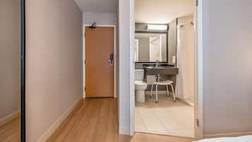 A hotel hallway with a wooden floor, a door leading to a bathroom with a sink, toilet, and mirror.
