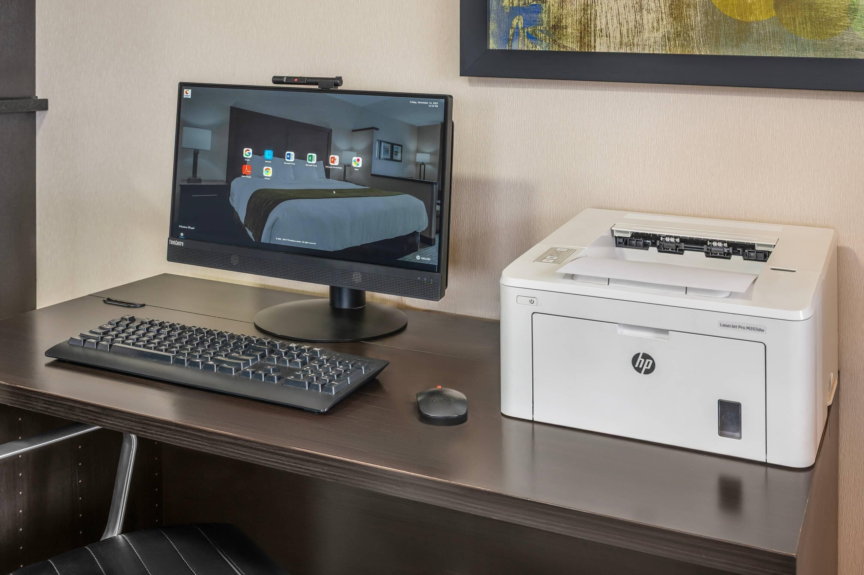A hotel room with a bed, a desk with a computer, a printer, and a chair.