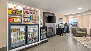 A hotel lobby with snack vending machines, a refrigerator with beverages, a flat-screen TV, and a seating area.