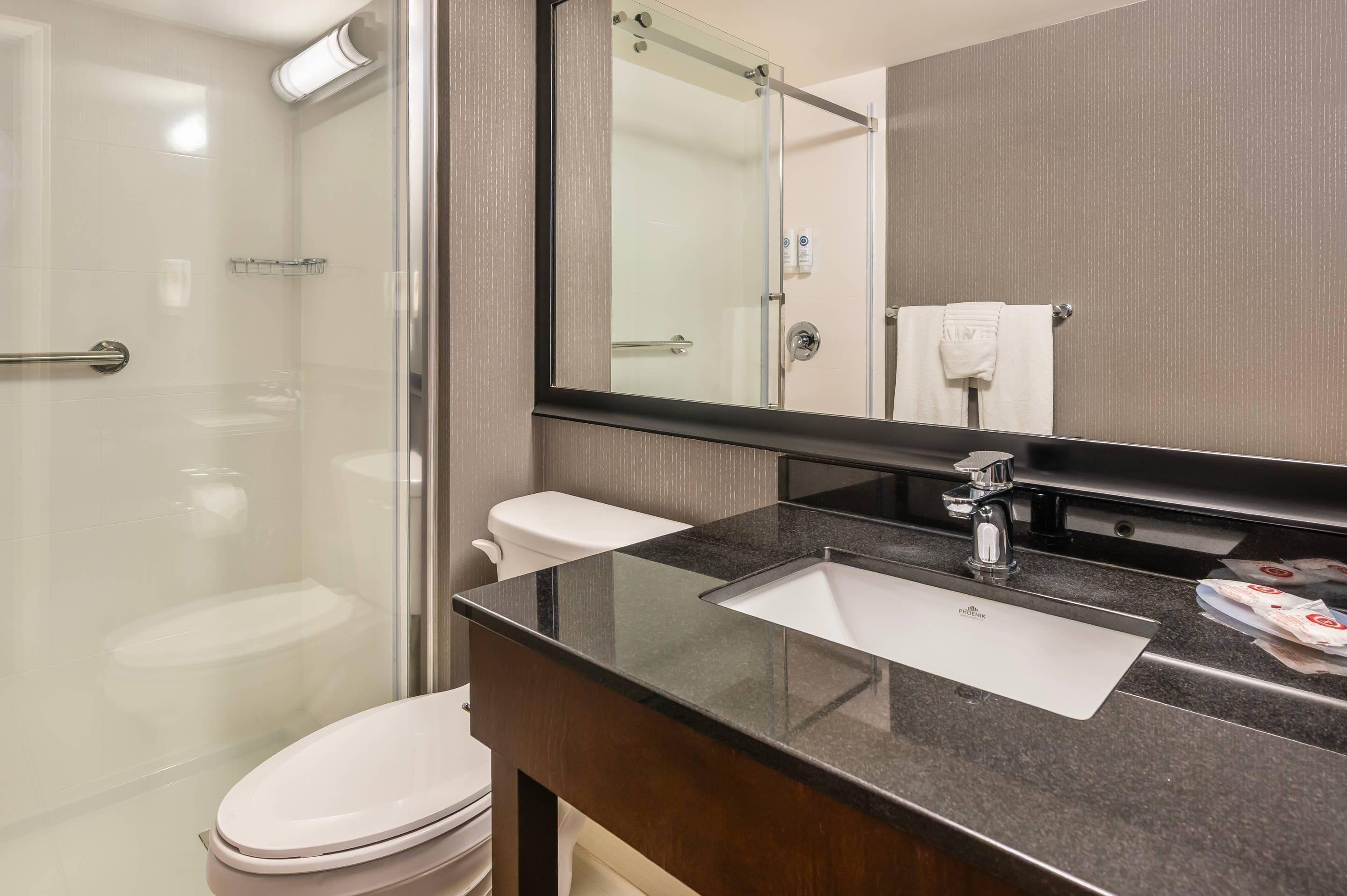 Un baño moderno con ducha de vidrio, inodoro blanco y tocador con lavamanos y espejo.