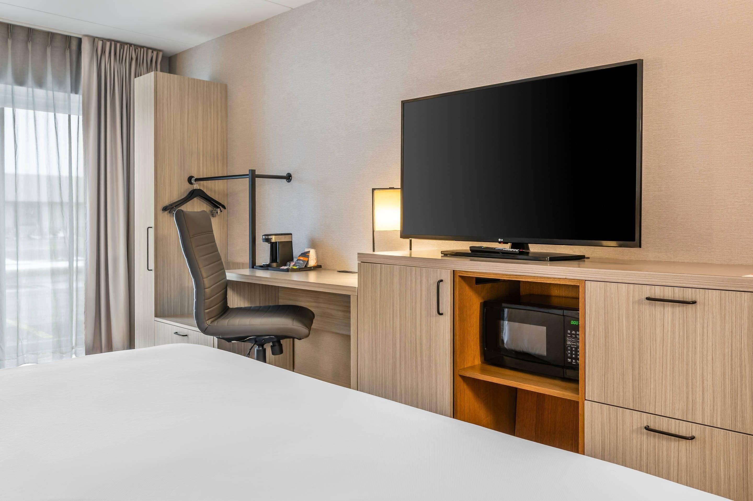 Una habitació d'hotel amb un llit, un escriptori amb una cadira, una televisió, un microones i un armari.