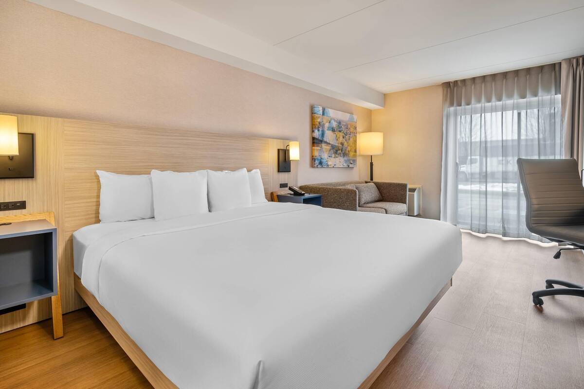 A hotel room with a large bed, a desk, a chair, a lamp, and a painting on the wall.