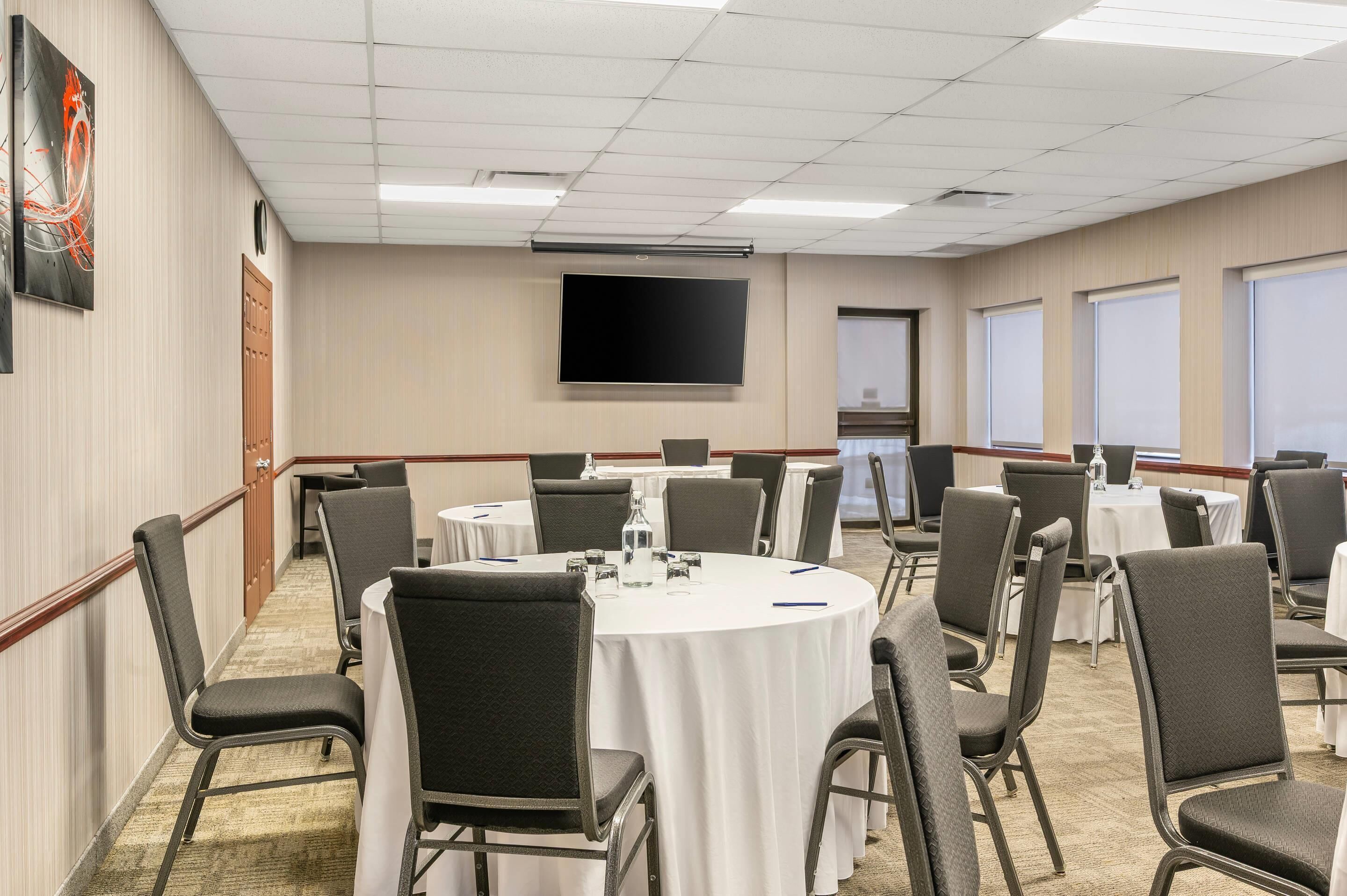 A conference room with round tables, chairs, a projector screen, and a large window.