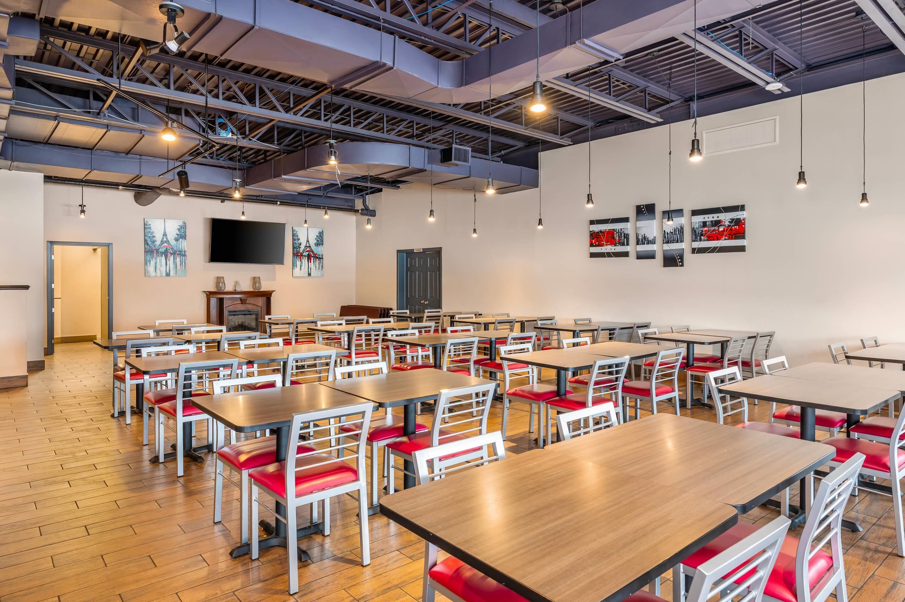 A spacious dining area with multiple tables and chairs, a flat-screen TV mounted on the wall, and a fireplace.