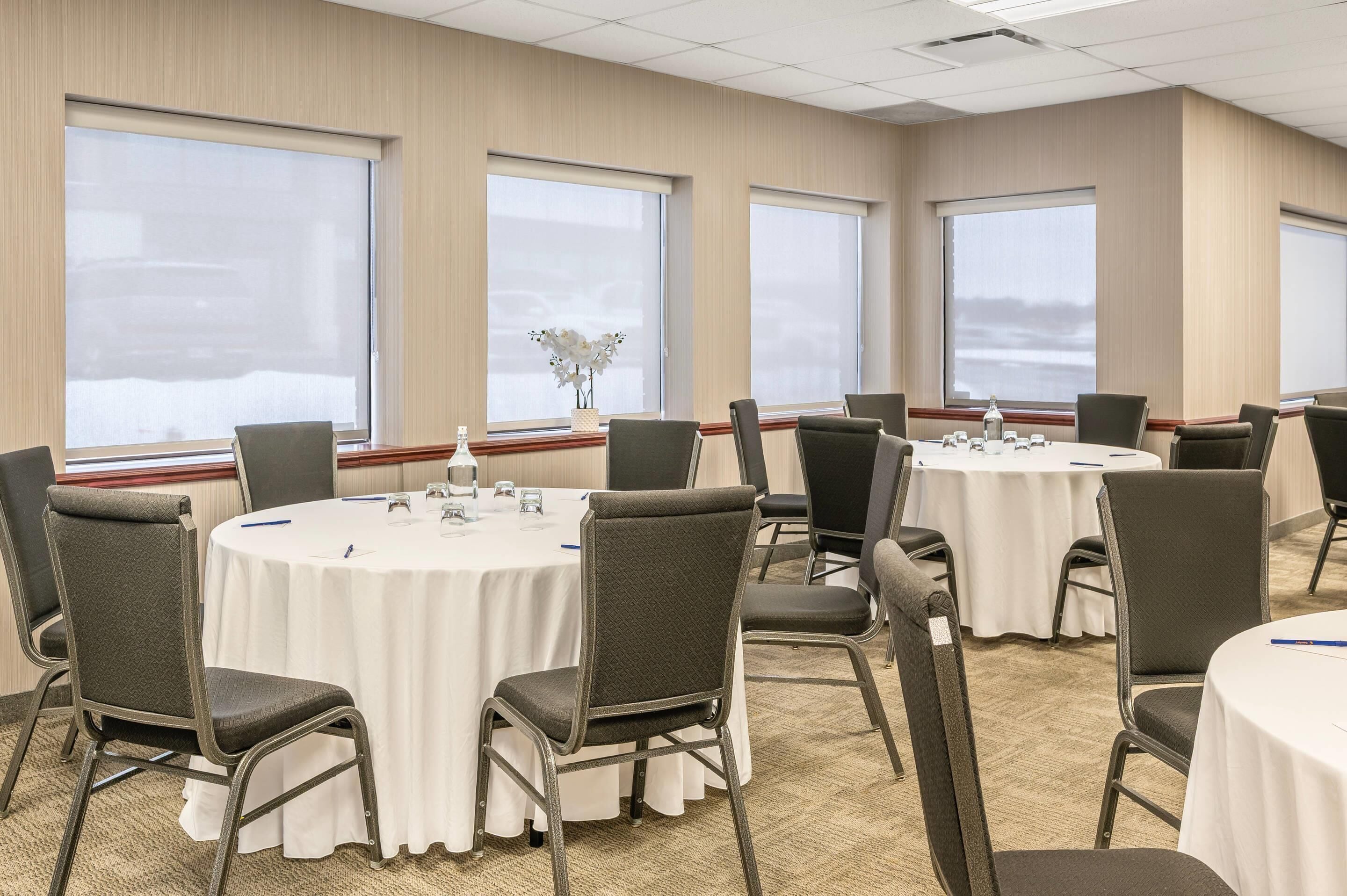 Un salón de conferencias con mesas redondas, sillas y ventanas amplias.
