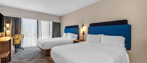 A hotel room with two beds, a desk, a chair, and a large window with curtains.