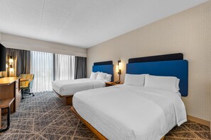 A hotel room with two beds, a desk, a chair, and a large window with curtains.