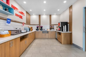 A modern kitchen with a 'HAPPY BREAKFAST STARTS HERE' sign, a bakery section, and a coffee station.